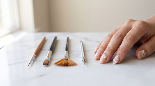 Pinceles de nail art profesionales: liner, plano, abanico y punteador junto a uñas con diseño pintado a mano