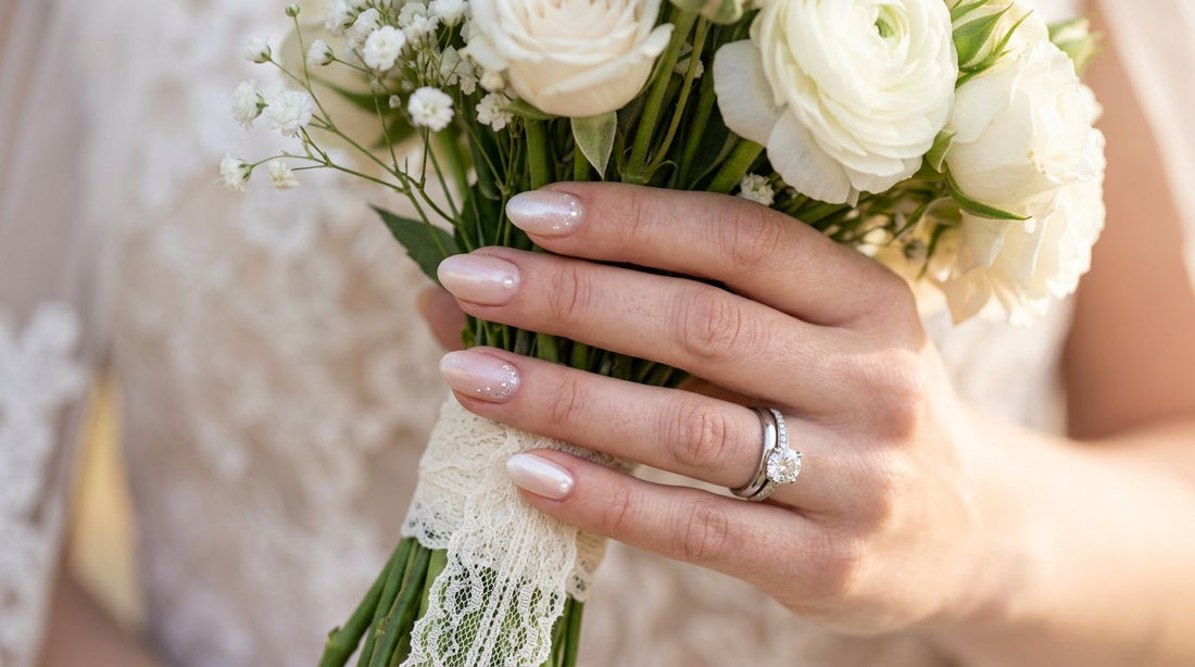 Manicura de novia 2026: uñas nude perladas con brillo sutil sosteniendo ramo de flores blancas