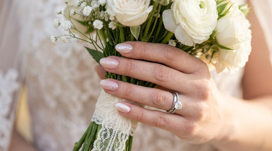 Manicura de novia 2026: uñas nude perladas con brillo sutil sosteniendo ramo de flores blancas