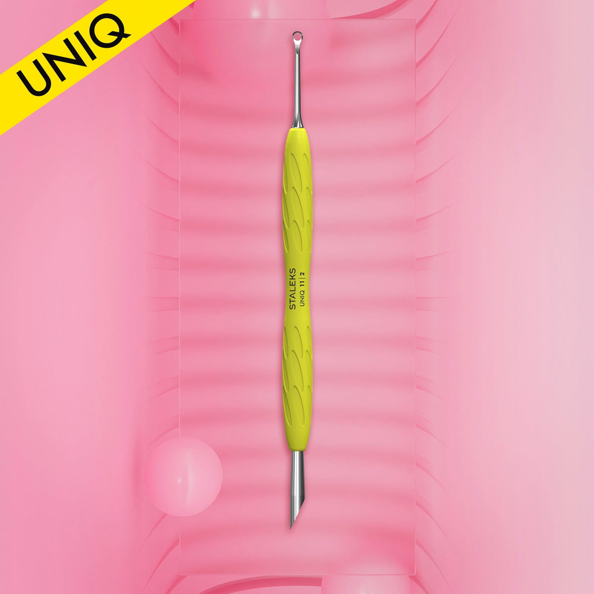 Empujador de cutículas Staleks UNIQ 11 Gummy con mango de silicona amarillo sobre fondo rosa